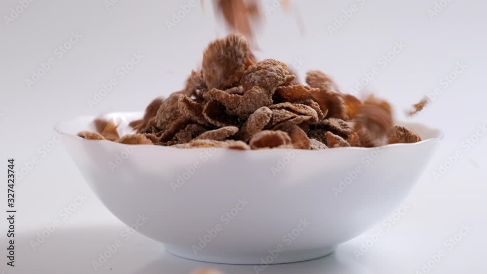 Natural whole grain wheat flakes are falling to white bowl. Healthy breakfast concept. Plate with multigrain flakes on white background Slow motion Natural whole grain wheat flakes are falling to white bowl. Healthy breakfast concept. Plate with multigrain flakes on white background Slow motion