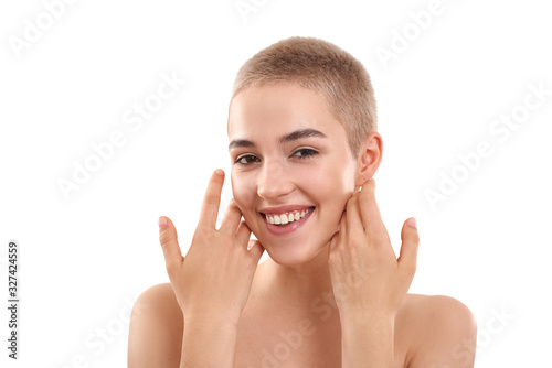 Glowing skin. Portrait of a beautiful smiling blond woman with short hair and nude make up touching her cheeks with hands and looking at camera