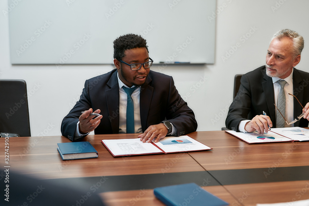 Talking about business. Successful business people in formal wear discussing something while sitting together at office desk. Partners working together in the modern office Talking about business. Successful business people in formal wear discussing something while sitting together at office desk. Partners working together in the modern office