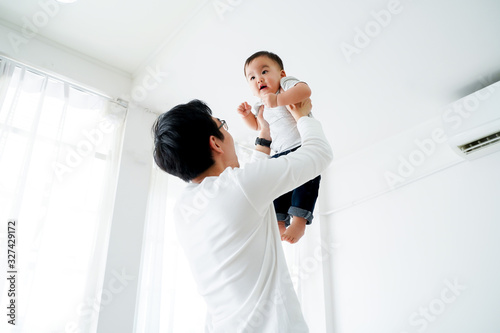 Young adult 30s Asian father lifting his little own son up flying in the air in bedroom at home. Family time and fatherhood concept in Asia