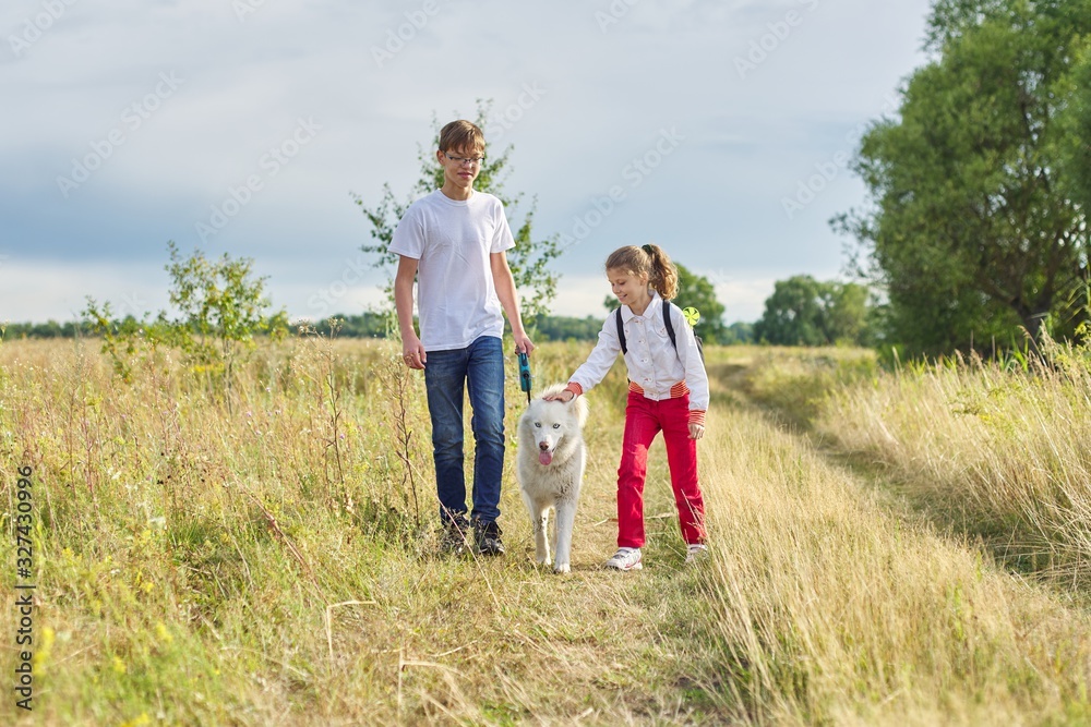 Children walking with white dog in meadow on autumn day Children walking with white dog in meadow on autumn day