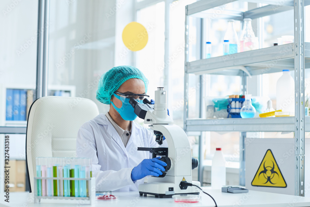 Portrait of female scientist looking in microscope while working on bio hazard research in laboratory, copy space Portrait of female scientist looking in microscope while working on bio hazard research in laboratory, copy space