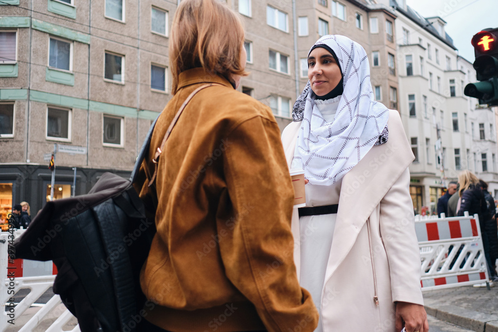 Young attractive Arabic woman in hijab talking with friend during walk around city street