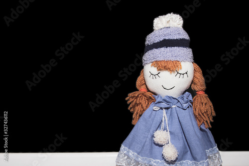 Handmade doll smiling in purple hat and dress on black background