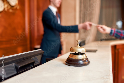 Always hear you. Young executive at the reception desk of a hotel working in the background. Focus on a service bell