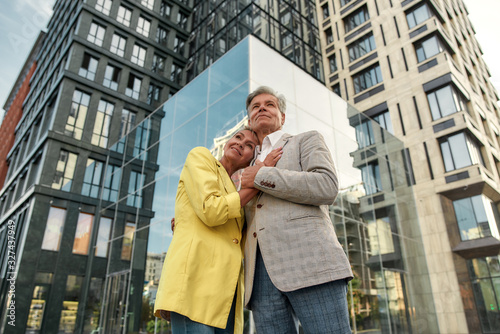 I can't imagine life without you. Happy middle-aged couple holding hands and embracing while standing against modern glass building © Svitlana
