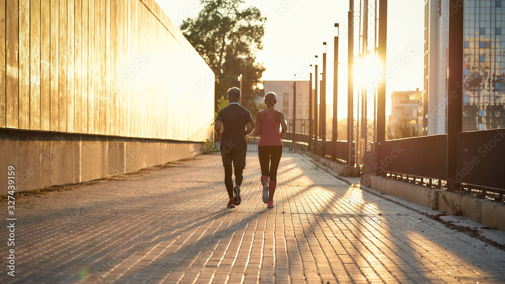 Early morning. Full length of a couple in sport clothing running together through the city street Early morning. Full length of a couple in sport clothing running together through the city street