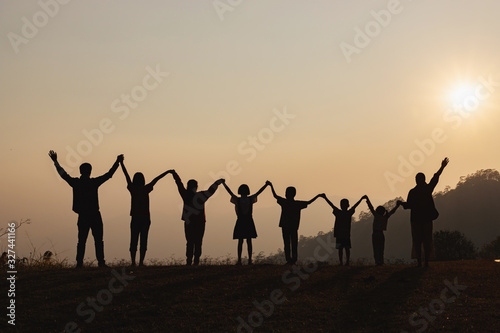 Silhouette of happy family standing with raised hands on the mountain at the sunset time.