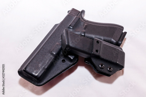 A black pistol in a plastic holster with a loaded magazine holster on a white background