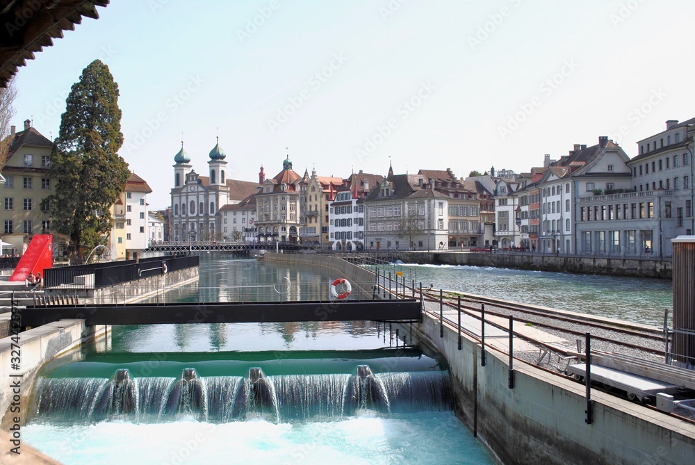 Nadelwehr Luzern is a 19th-century needle dam on Reuss River uses wooden posts to control the water flow from Lake Lucerne in Lucerne, Switzerland. The Jesuit church with onion domes in background. 