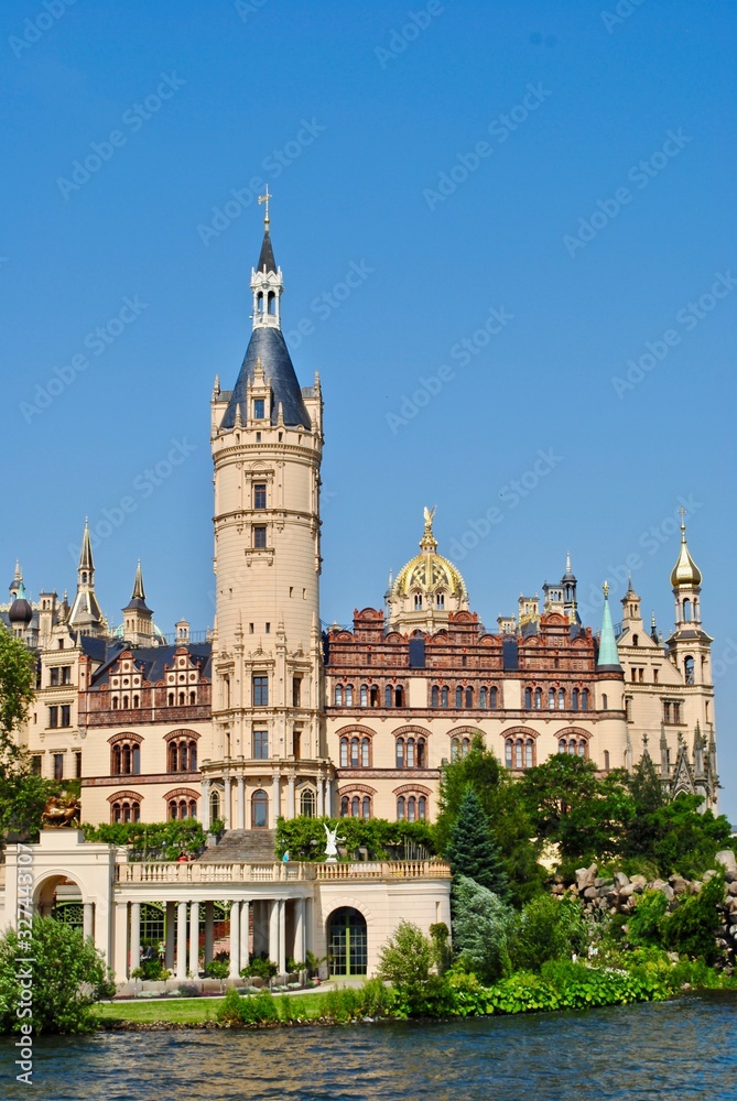 The Schwerin Palace, as seen from the water. The castle is a palatial schloss located in the city of Schwerin. It is situated on an island or islet in the city's main lake, the Lake Schwerin. 