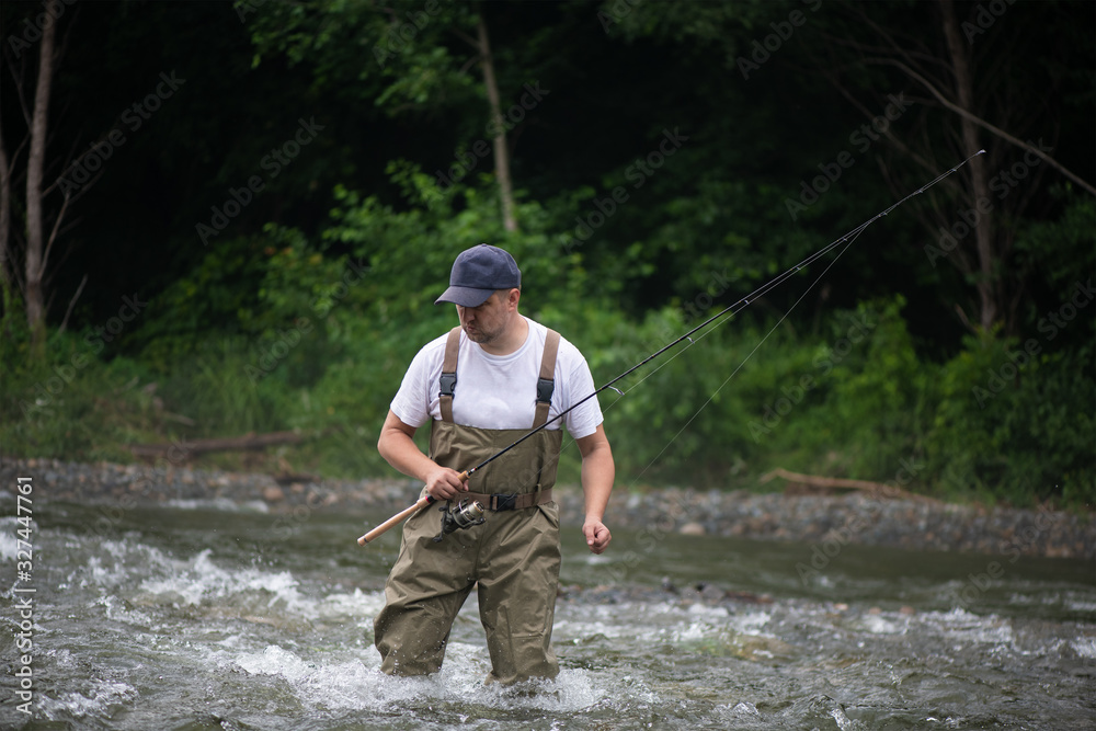 A fisherman with a fishing rod crosses a mountain river.