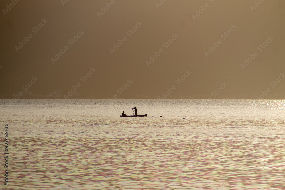 Two men on a boat fishing during the dawn