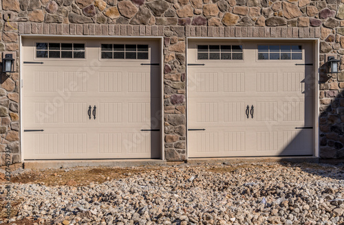 Two single car classic insulated steel panel garage door framed with architectural stone to add accent, with transom light windows divided by muntins grills on a new American home under construction