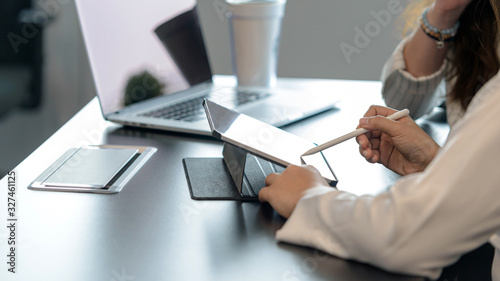 Two young business women sitting at table. First woman holding stylus pen and point to digital tablet screen. close up side view. photo