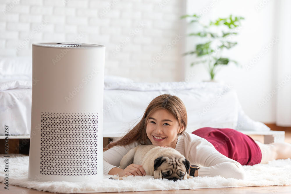Woman playing with Dog Pug Breed and Air purifier in cozy white bed room  for filter and cleaning removing dust PM2.5 HEPA in home,for fresh air and  healthy life,Air Pollution Concept Photos