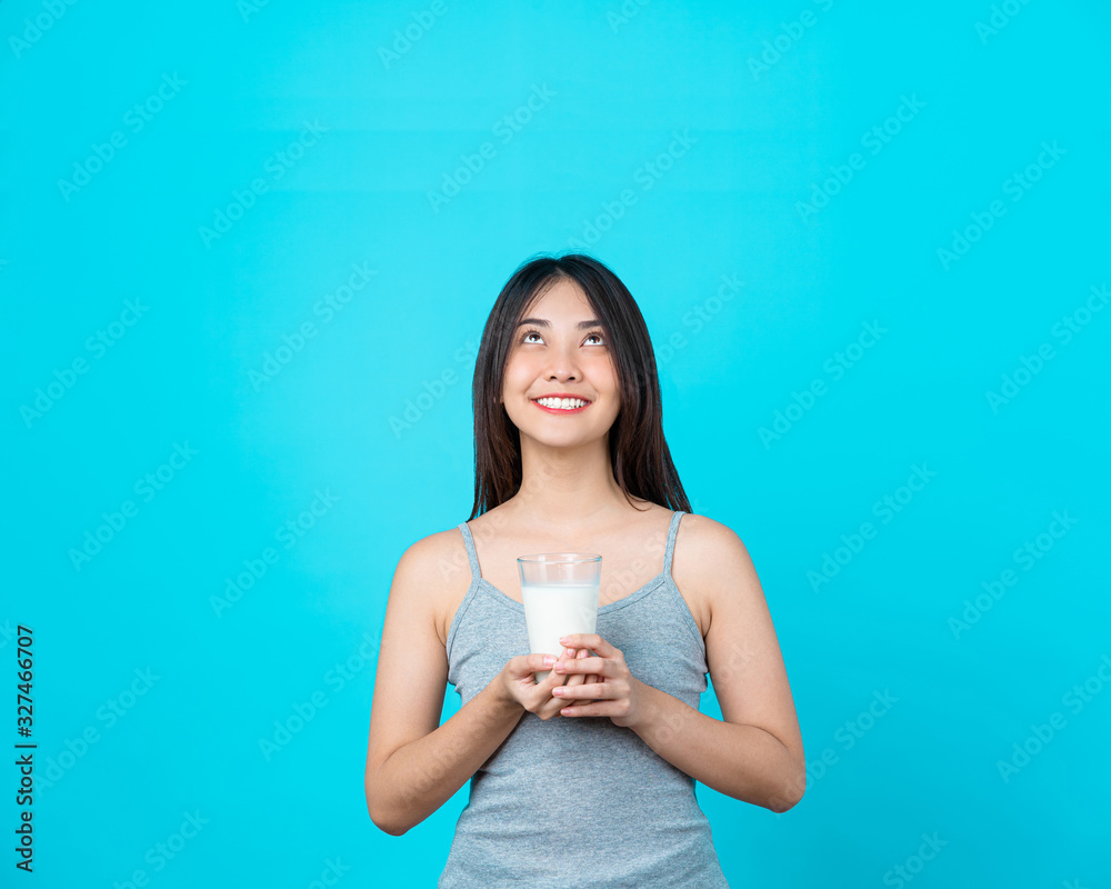 Attractive Asian young woman holding milk on isolated blue color background, weight loss and avoid junk food for dieting and Healthy