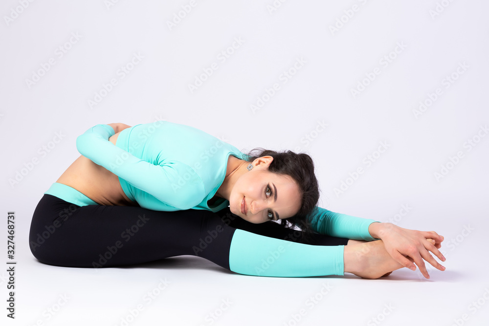 Fototapeta premium Attractive woman in styling and bright make-up in pants and top stretches on the floor, on a white isolated background. Pretty athlete for design and advertising.
