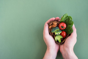 Healthy food for heart on green background. Man hands hold plate with vegetables, spinach and nuts. Diet, superfood and health concept. Top view, flat lay, copy space