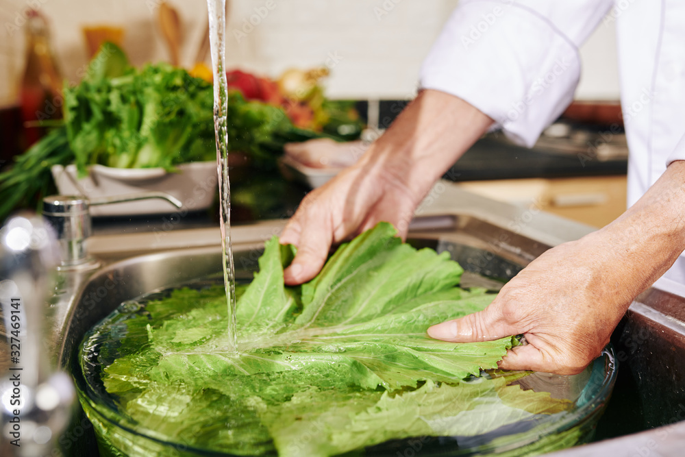 Hands of man washing lettuce in big bowl with water in kitchen sink