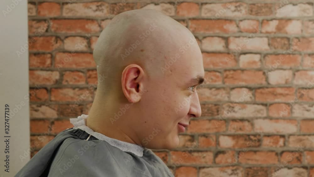 Bald man with shaved head sitting in barber chair in male salon. Profile view bald man after shave talking in barbershop. Portrait young man in hairdressing salon Bald man with shaved head sitting in barber chair in male salon. Profile view bald man after shave talking in barbershop. Portrait young man in hairdressing salon