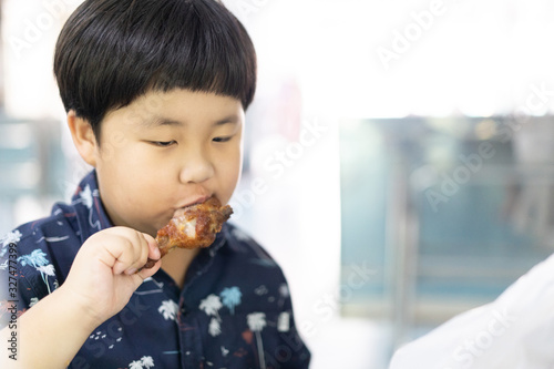 a fat Asian boy is eating a chicken.