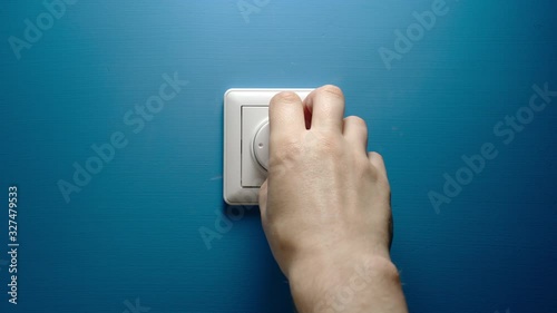 Male hand turns dimmer button on a blue wall