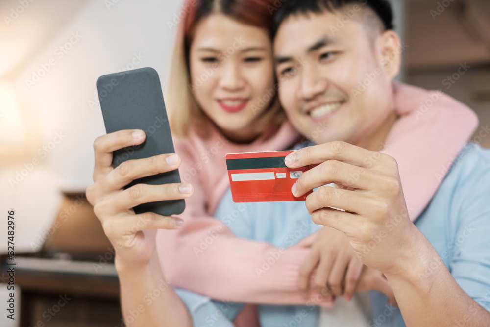 Asian couple use mobile phone shopping online with credit card together in living room at home.couple in home concept Asian couple use mobile phone shopping online with credit card together in living room at home.couple in home concept