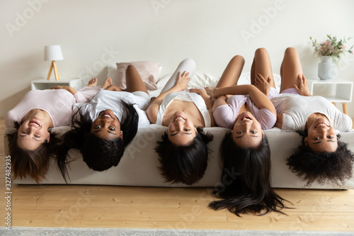Happy diverse girls lying on bed upside down, having fun