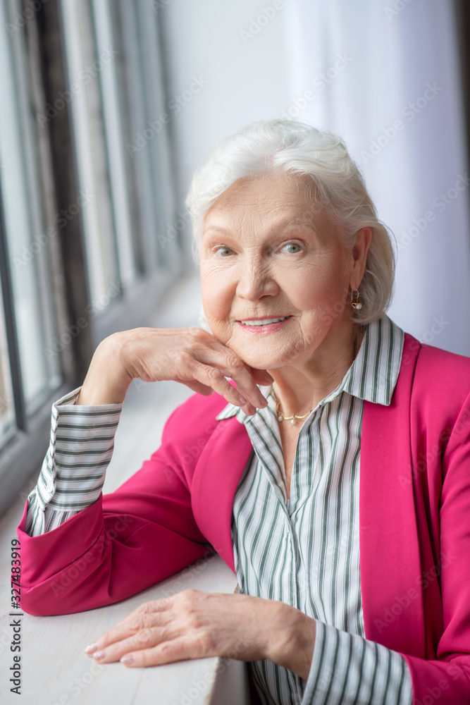 Grey-haired smiling lady standing near the window Grey-haired smiling lady standing near the window