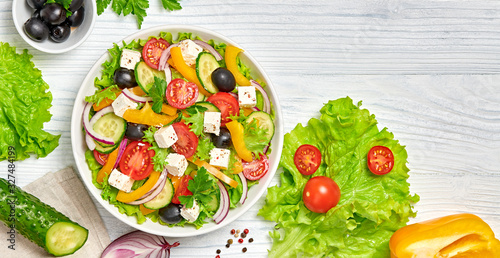 Greek salad with cucumeber, olives, feta cheese, cherry tomatoes, bell pepper, onion and lettuce. Diet, vitamin food. Healthy vegetarian meal concept. Tasty salad in bowl on white wood, top view.