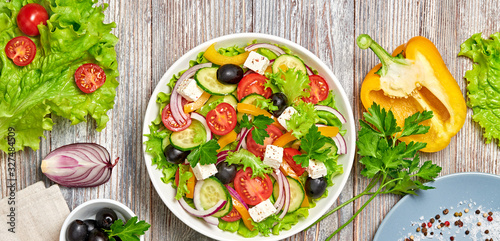 Greek salad with cucumeber, olives, feta cheese, cherry tomatoes, bell pepper, onion and lettuce. Diet, vitamin food. Healthy vegetarian meal concept. Tasty salad in bowl on wood, flat lay.