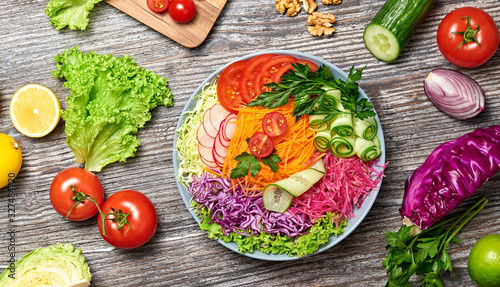 Rainbow salad with tomato, lettuce, cucumber, red cabbage, carrot, radish. Paleo diet, healthy vegan and balanced food concept. Fresh mix green leaves homemade vegetable salad on wood, top view