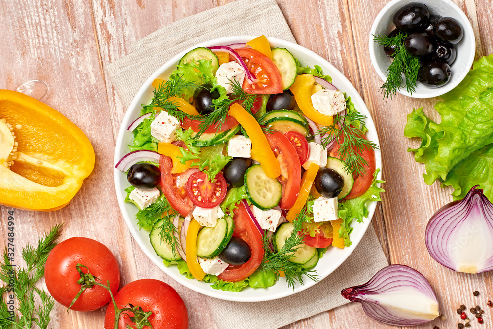 Greek salad with cucumeber, olives, feta cheese, cherry tomatoes, bell pepper, onion and lettuce. Diet, vitamin food. Healthy vegetarian meal concept. Tasty salad in bowl on wood, top view. Greek salad with cucumeber, olives, feta cheese, cherry tomatoes, bell pepper, onion and lettuce. Diet, vitamin food. Healthy vegetarian meal concept. Tasty salad in bowl on wood, top view.