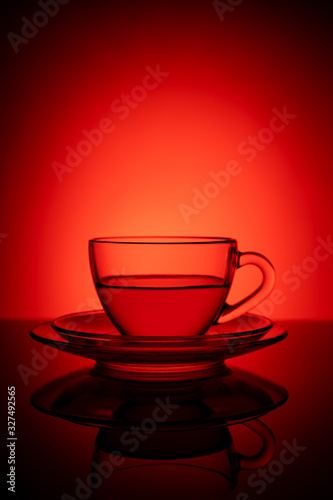 Glass cup of tea on a glass saucer with reflection, with a gradient of black, and red background. Concept, healthy and stylish lifestyle. Magazine and commercial photo with place for text or design