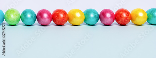 Row of brightlypainted glossy Easter eggs on light blue background. Easter banner. Copy space  low angle.