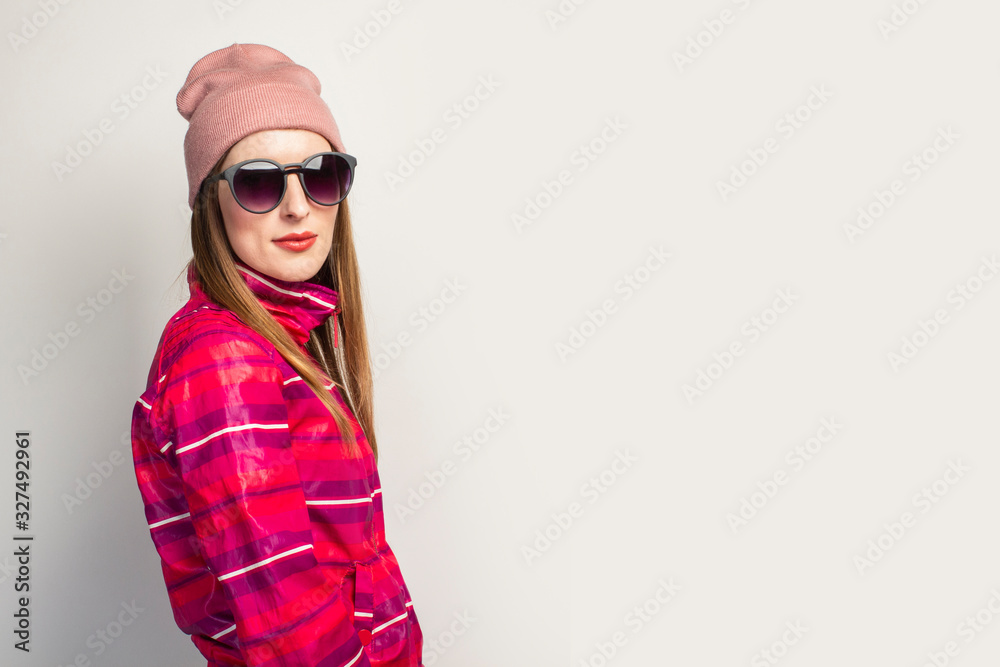 Friendly emotional Young woman with glasses, a hat and a pink sports jacket with a serious face on a white background with copy space. Concept modern trendy style. Face expression. Banner Friendly emotional Young woman with glasses, a hat and a pink sports jacket with a serious face on a white background with copy space. Concept modern trendy style. Face expression. Banner