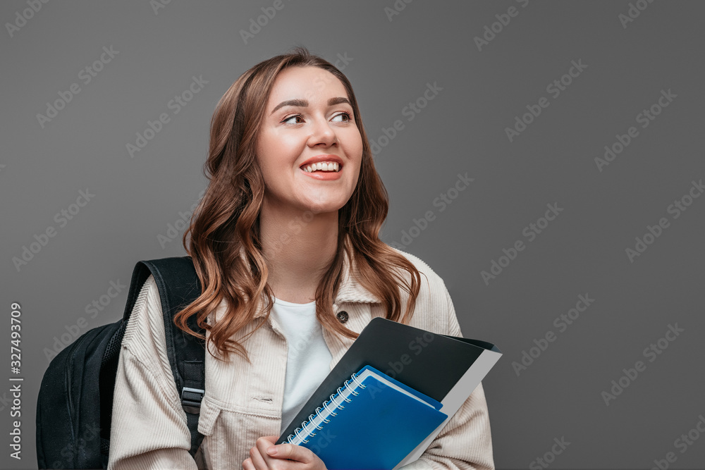 Happy girl student laughs and smiles and looking away holding a notebook isolated over dark grey background, copy space. University entrance exams concept Happy girl student laughs and smiles and looking away holding a notebook isolated over dark grey background, copy space. University entrance exams concept