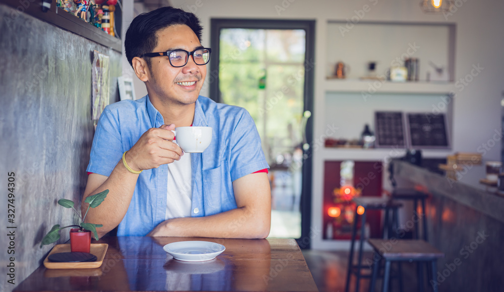 Attractive Asian man drinking coffee at the table in coffee shop. Film tone effected. Attractive Asian man drinking coffee at the table in coffee shop. Film tone effected.