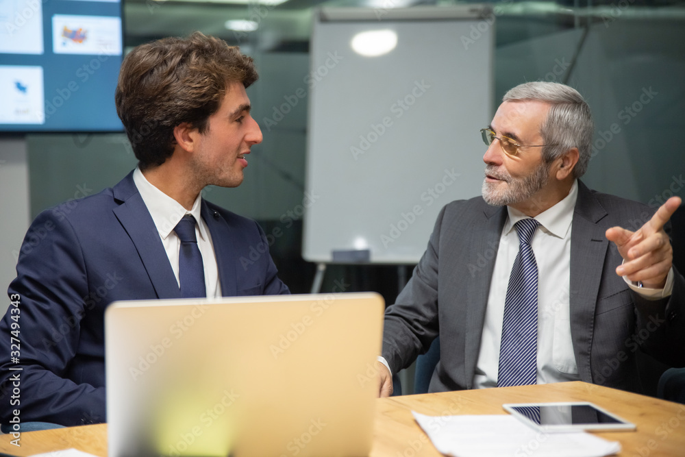 Front view of confident businessmen communicating. Two office employees sitting at table and working over new project. Business, teamwork concept Front view of confident businessmen communicating. Two office employees sitting at table and working over new project. Business, teamwork concept