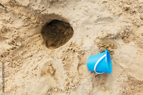 un seau en plastique bleu et un trou sur une plage de sable en été. Loisir d'enfant  photo