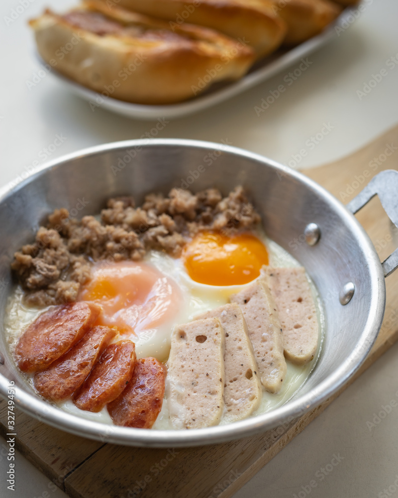 Fried eggs in a pan with meat on the wooden plate. The famous breakfast with Banh Mi - Vietnamese bun with meat. Fried eggs in a pan with meat on the wooden plate. The famous breakfast with Banh Mi - Vietnamese bun with meat.
