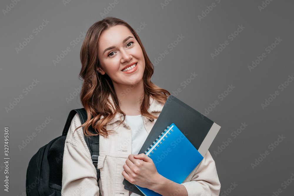 Happy girl student in bright clothes holding a notebook, notepad, a folder in her hands, smiling and looking at the camera on a dark grey background, copy space for text Happy girl student in bright clothes holding a notebook, notepad, a folder in her hands, smiling and looking at the camera on a dark grey background, copy space for text