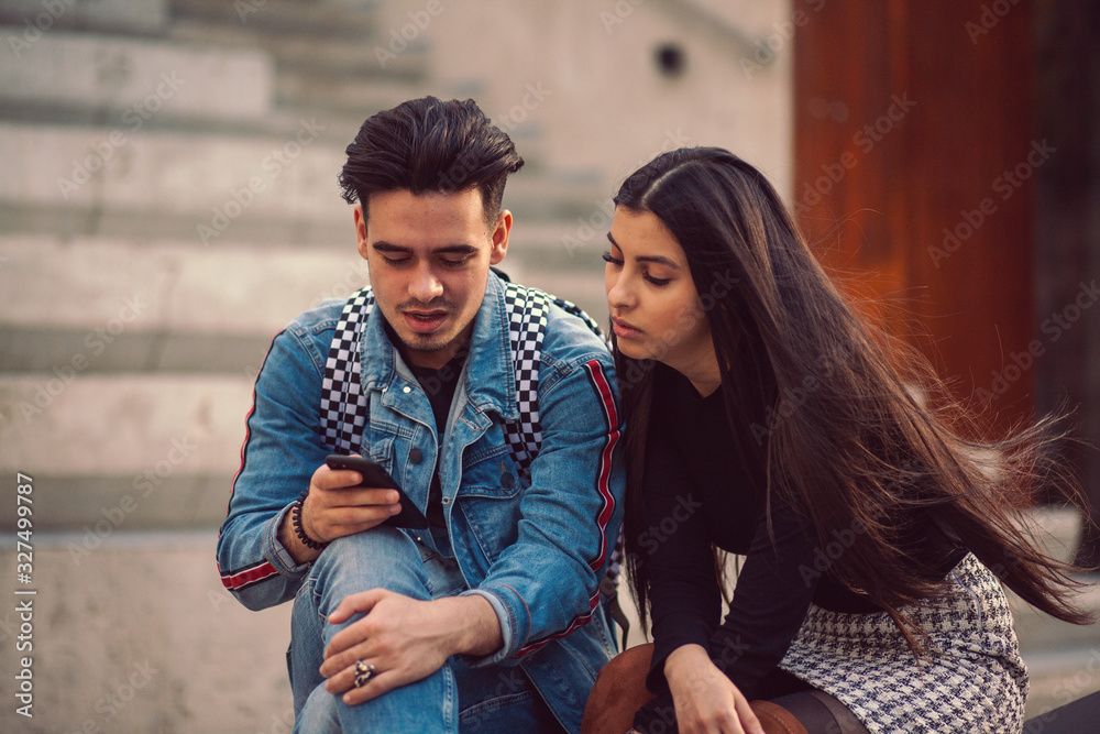 Portrait of young couple sit on a park bench and look at photos on a smartphone