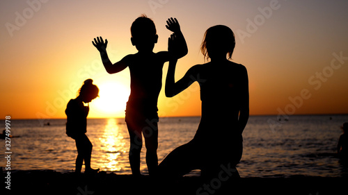 Happy family mother with two children on vacation at the beach during amazing sunset.