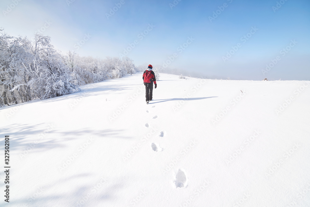 Young trekker in a red clothes is enjoying life and winter views in mountains during sunny winter day.