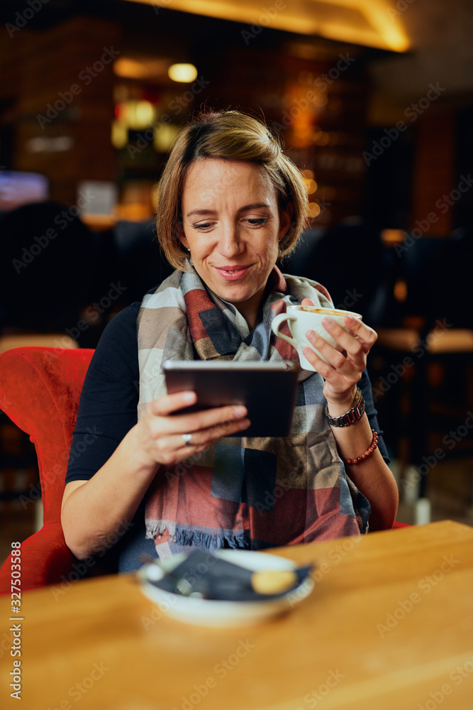 Beautiful Caucasian woman with coffee looking at her tablet	