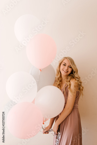 Beautiful young smiling blonde woman with white gray and pink balloons on a light background