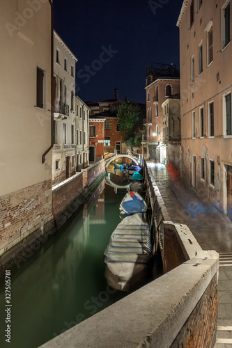 Narrow canal with boats and vintage houses at dusk. Venice city at night