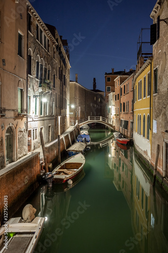 Narrow canal with boats and vintage houses at dusk. Venice city at night